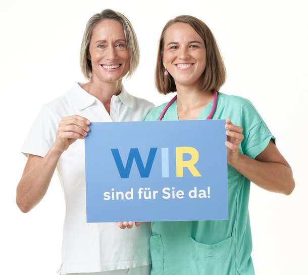 Mitarbeiterinnen halten ein Schild mit der Aufschrift "Wir sind für Sie da!"