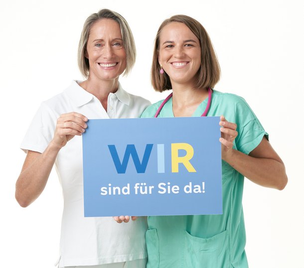 Mitarbeiterinnen halten ein Schild mit der Aufschrift "Wir sind für Sie da!"